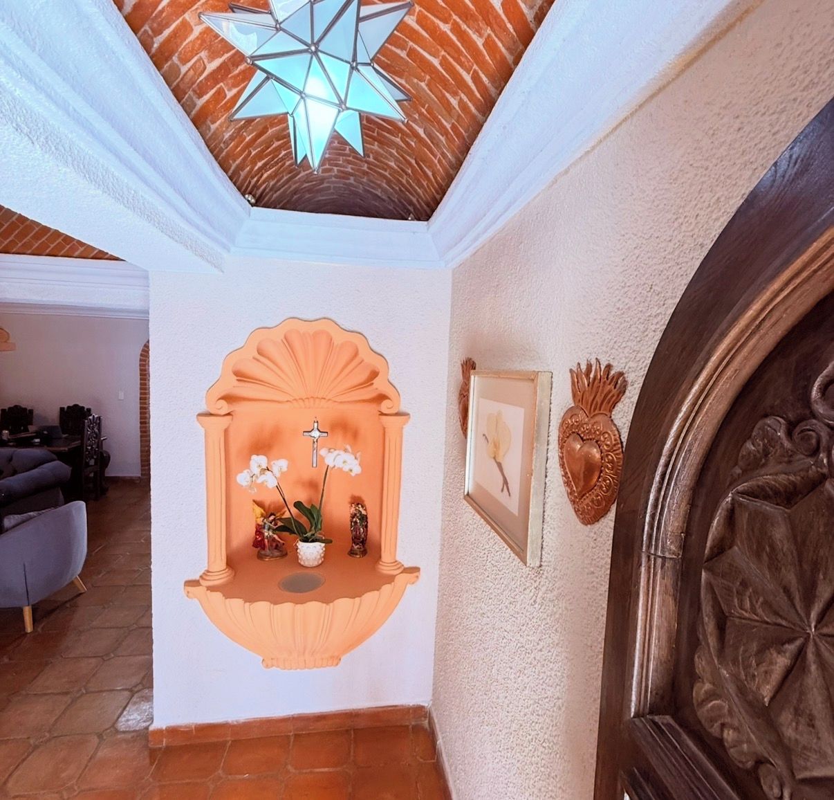 A hallway with a decorative alcove featuring a cross, orchids, and a heart-shaped ornament.