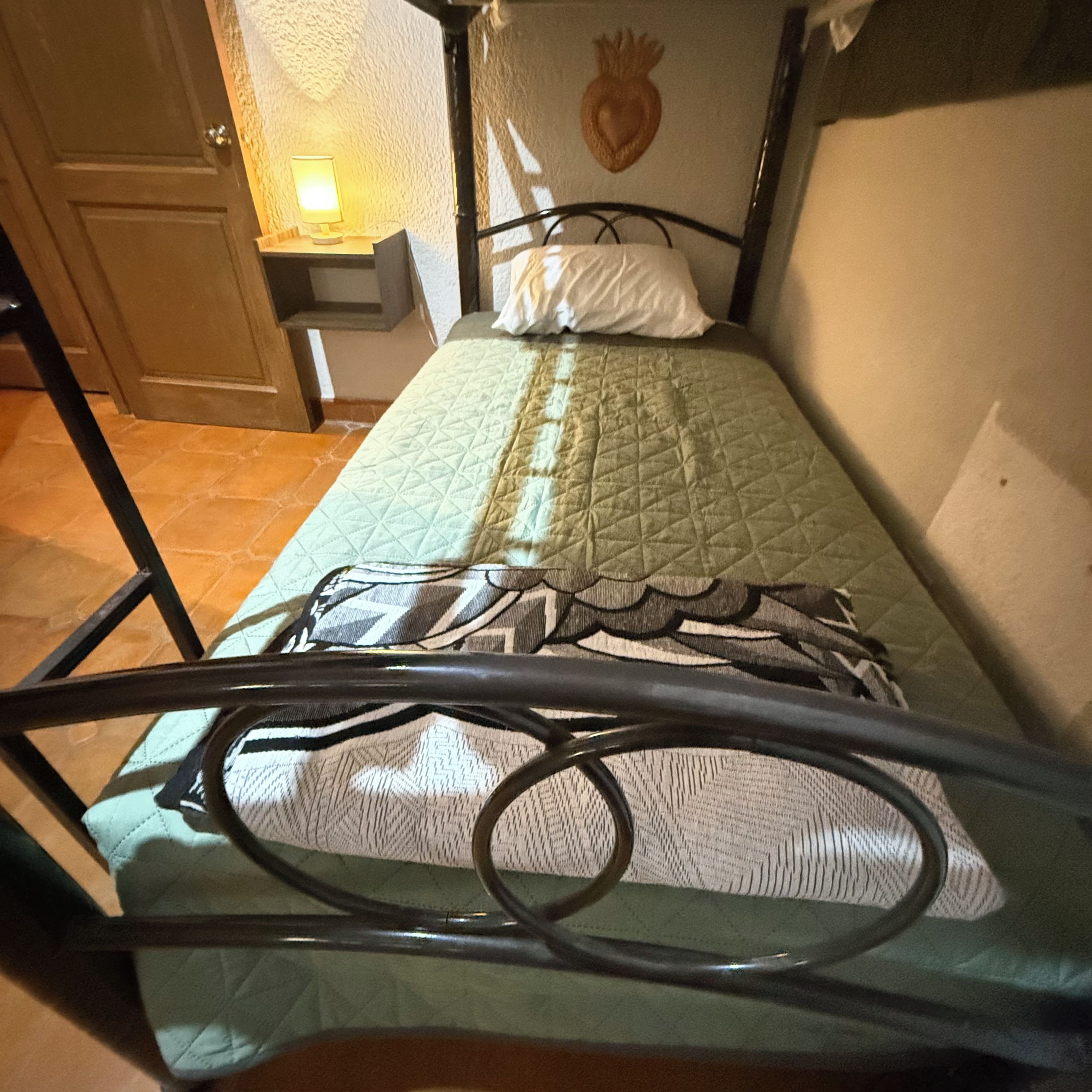 A single bed with a quilted green bedspread, a pillow, and a headboard with a heart-shaped decoration.