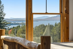 Ein Fenster mit Holzrahmen und Blick auf See und Wald.