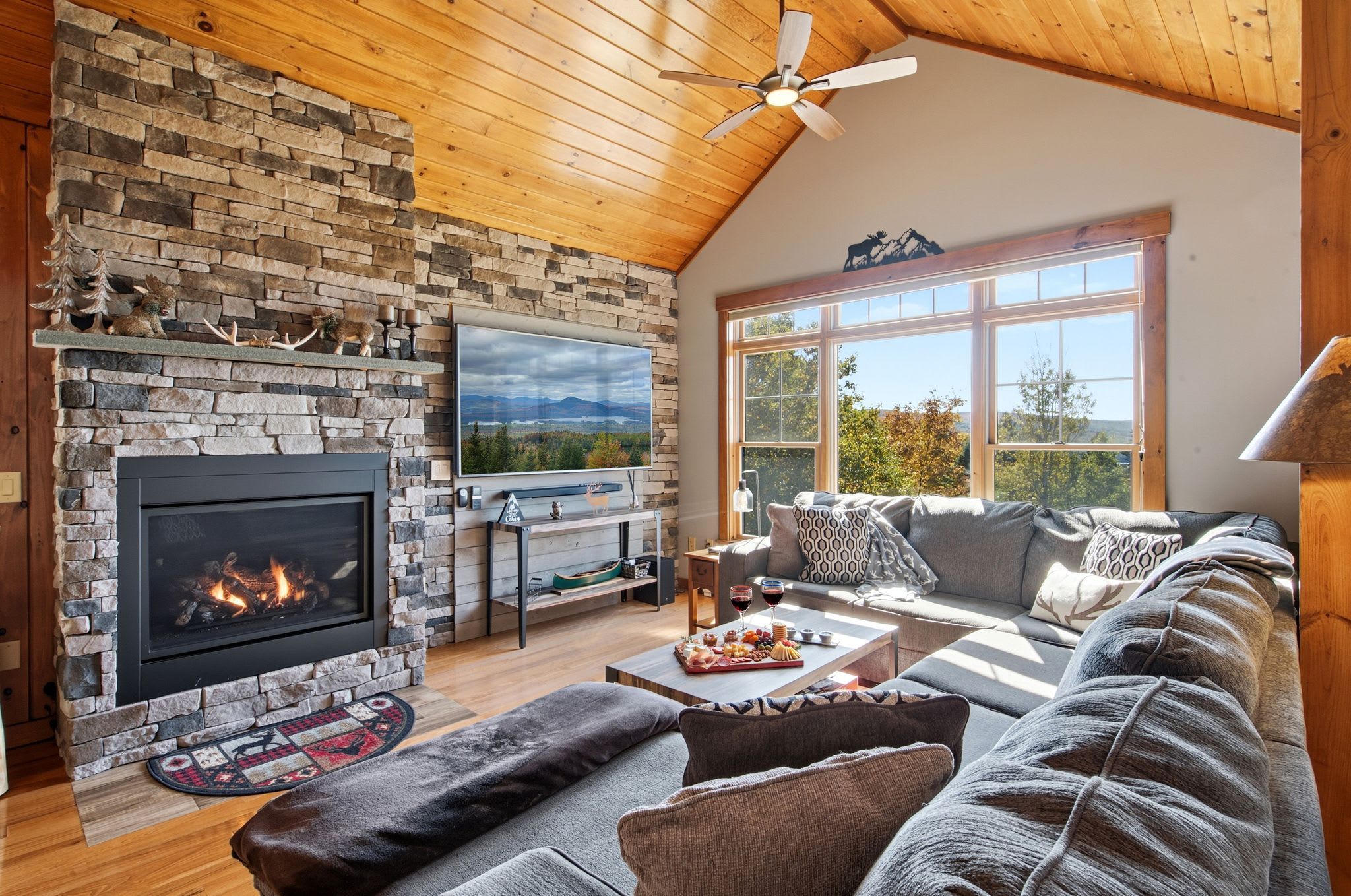 A cozy living room with a stone fireplace, a large window, and a comfortable seating area.