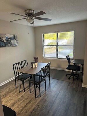 Un espace repas comprenant une table, des chaises, un ventilateur de plafond et une fenêtre avec des stores.
