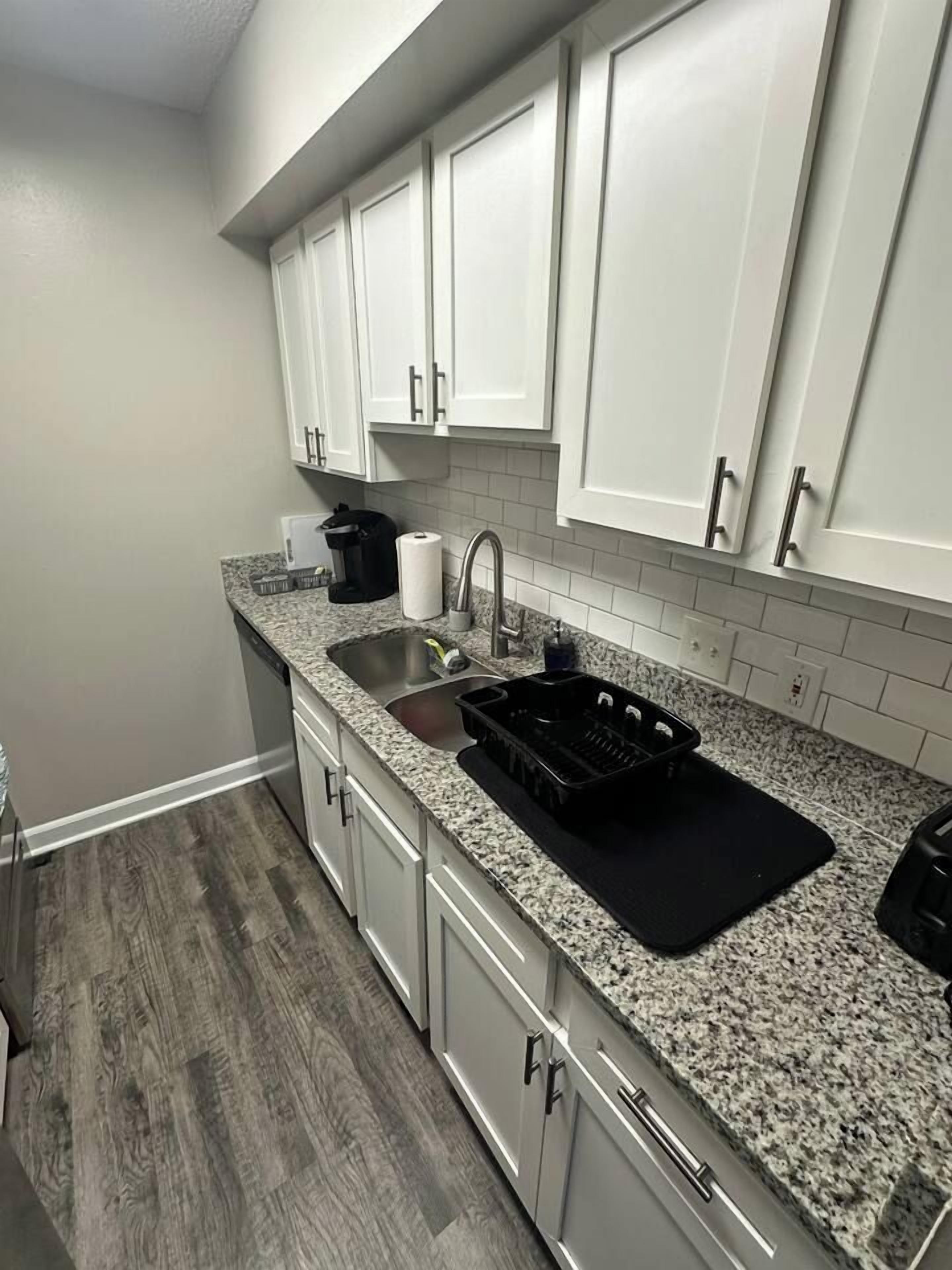 Una cocina con armarios blancos, encimera de granito, un lavabo y una bandeja negra.