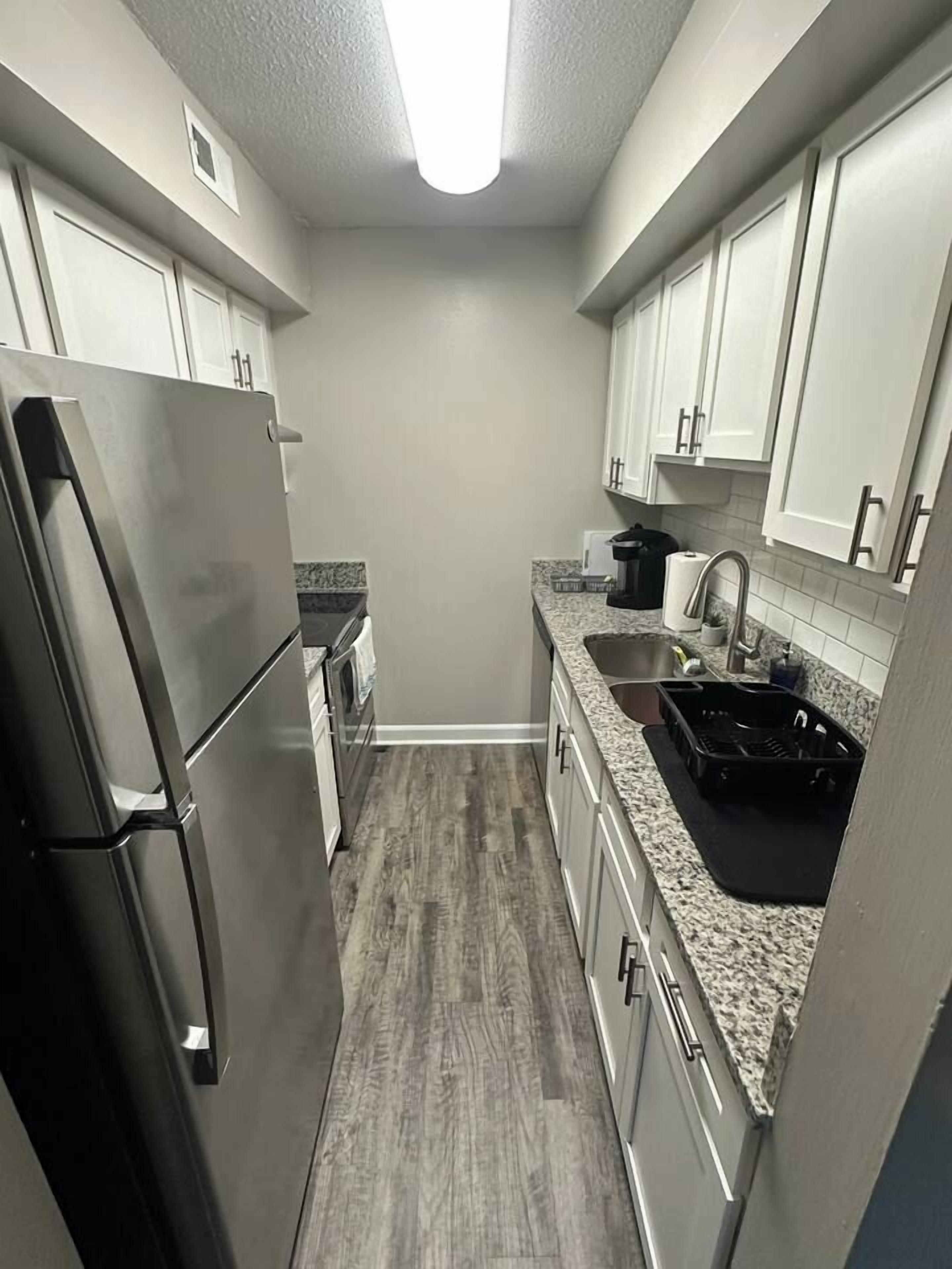 A compact kitchen with white cabinets, a stainless steel refrigerator, a granite countertop, and a black sink.