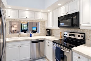A modern kitchen with white cabinetry, a stainless steel dishwasher, a black stove, and a microwave. - Lakefront Shorewalk Palms Condo Easy Does It (Bradenton)