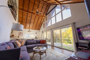A spacious living room with a large sectional sofa, a round coffee table, and a television on the wall. - The Catskill Oasis · Private Pond, Creek, Trails, Hot Tub (Napanoch)