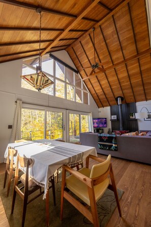 A spacious room with a high ceiling, a dining table with chairs, a sofa, and a television. - The Catskill Oasis · Private Pond, Creek, Trails, Hot Tub (Napanoch)