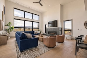 A spacious living room with a large fireplace, a blue sofa, leather armchairs, and a view of the outdoors. - New Luxury 4 bed | Hot Tub w/ Teton View | Targhee | AC (Driggs)