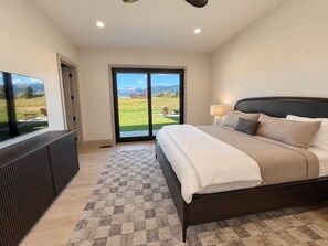 A bedroom with a bed, a TV, and a view of a grassy field through a sliding door. - New Luxury 4 bed | Hot Tub w/ Teton View | Targhee | AC (Driggs)