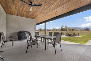 Une terrasse extérieure avec une table et des chaises, un barbecue et une vue sur un champ verdoyant et des montagnes.