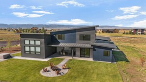 A modern two-story house with a patio area featuring outdoor seating. - New Luxury 4 bed | Hot Tub w/ Teton View | Targhee | AC (Driggs)