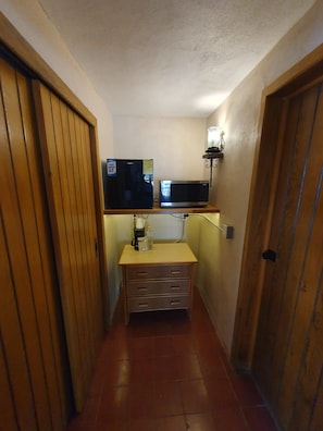 Ein schmaler Korridor mit einer Holztür links, einem kleinen Holzschrank mit Schubladen und einem an der Wand befestigten Flachbildfernseher rechts.