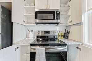 A modern kitchen with stainless steel appliances, white cabinetry, and a granite countertop. - Luxury New Home in Findlay Creek (Ottawa)
