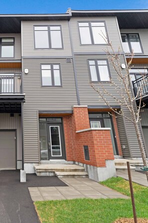 A multi-story residential building with a flat roof, large windows, and a brick accent wall. - Luxury New Home in Findlay Creek (Ottawa)