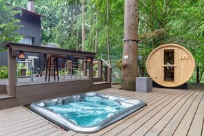 Un jacuzzi en una terraza de madera con un área de estar cubierta y una sauna.