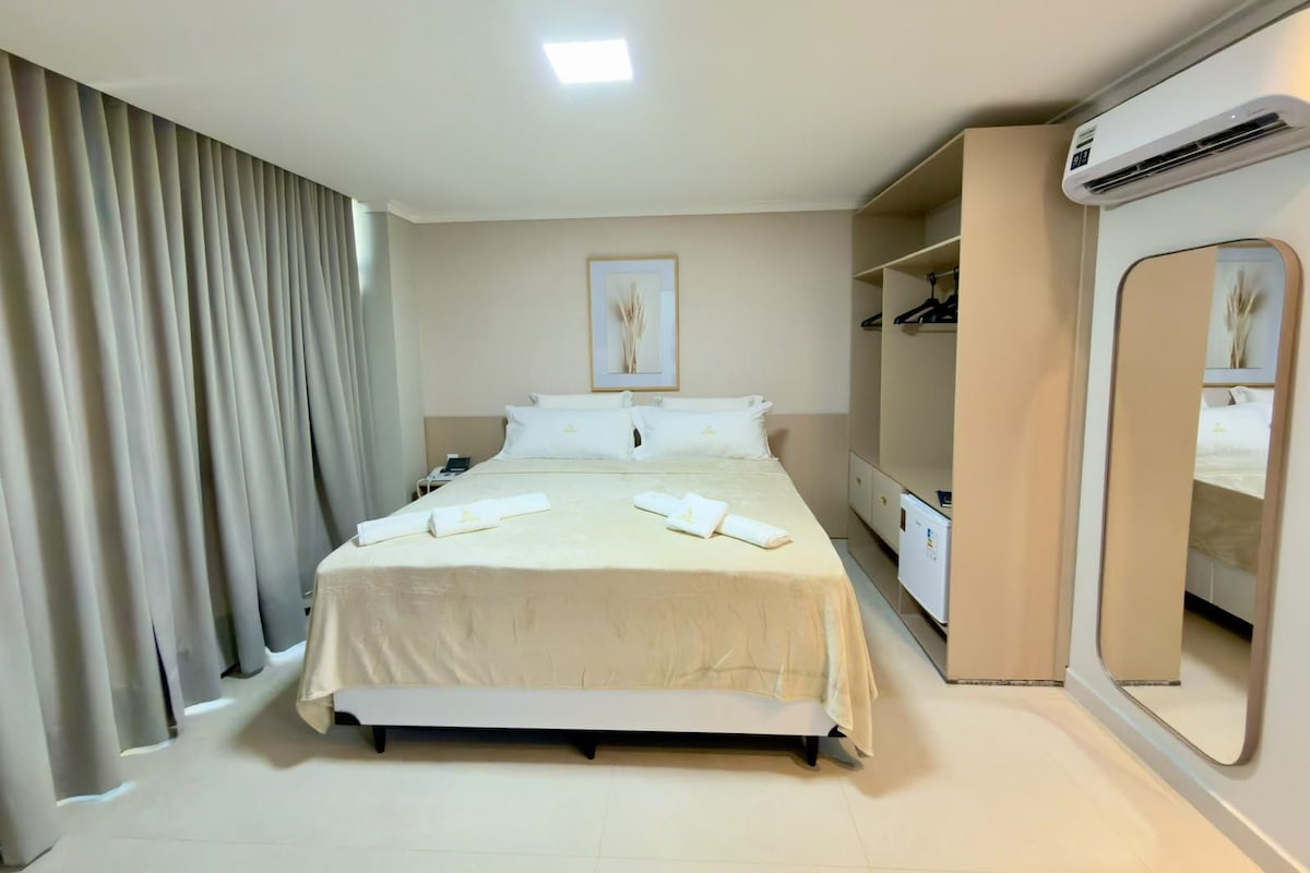 Una habitación de hotel con una cama, una mesita de noche, un espejo, un aire acondicionado y un armario.