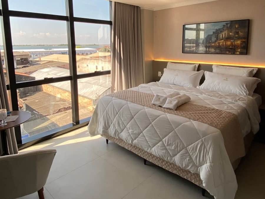 A hotel room with a large bed, a view of the cityscape, and a painting on the wall.