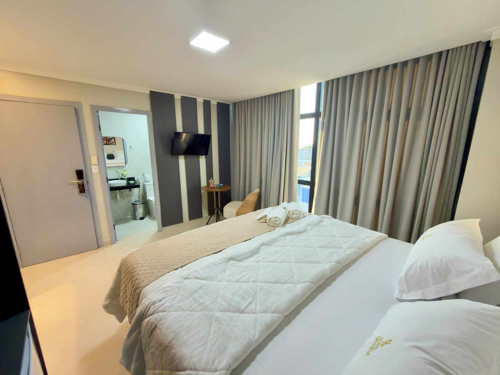 Ein Hotelzimmer mit Bett, Fernseher, einem kleinen Tisch und einem durchgegangenen Badezimmer.