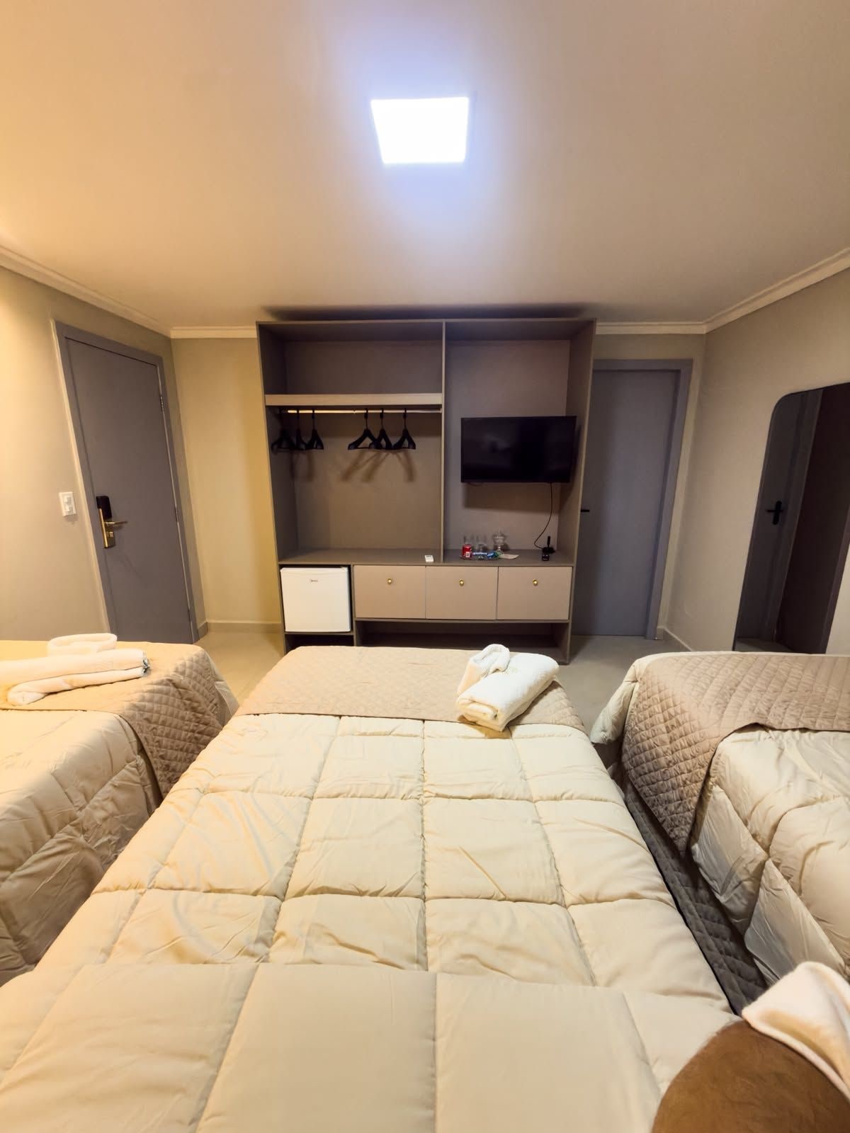 A hotel room with two beds, a TV, a wardrobe, and a small desk.