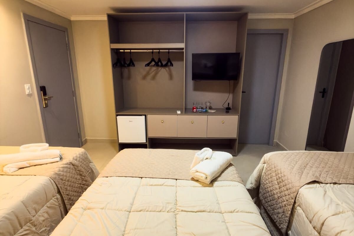 Habitación de hotel con dos camas, televisión, armario y un escritorio pequeño.