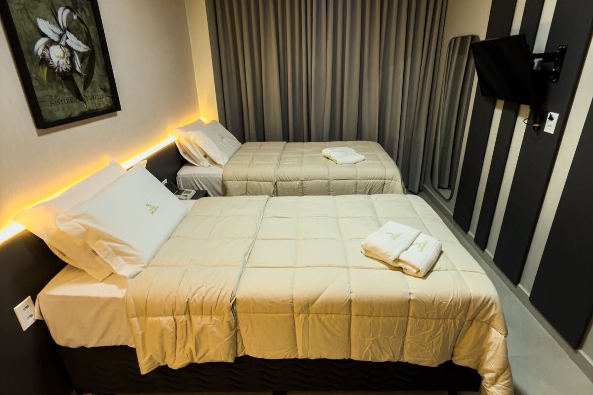 Habitación de hotel con dos camas, un cuadro en la pared y un televisor montado.