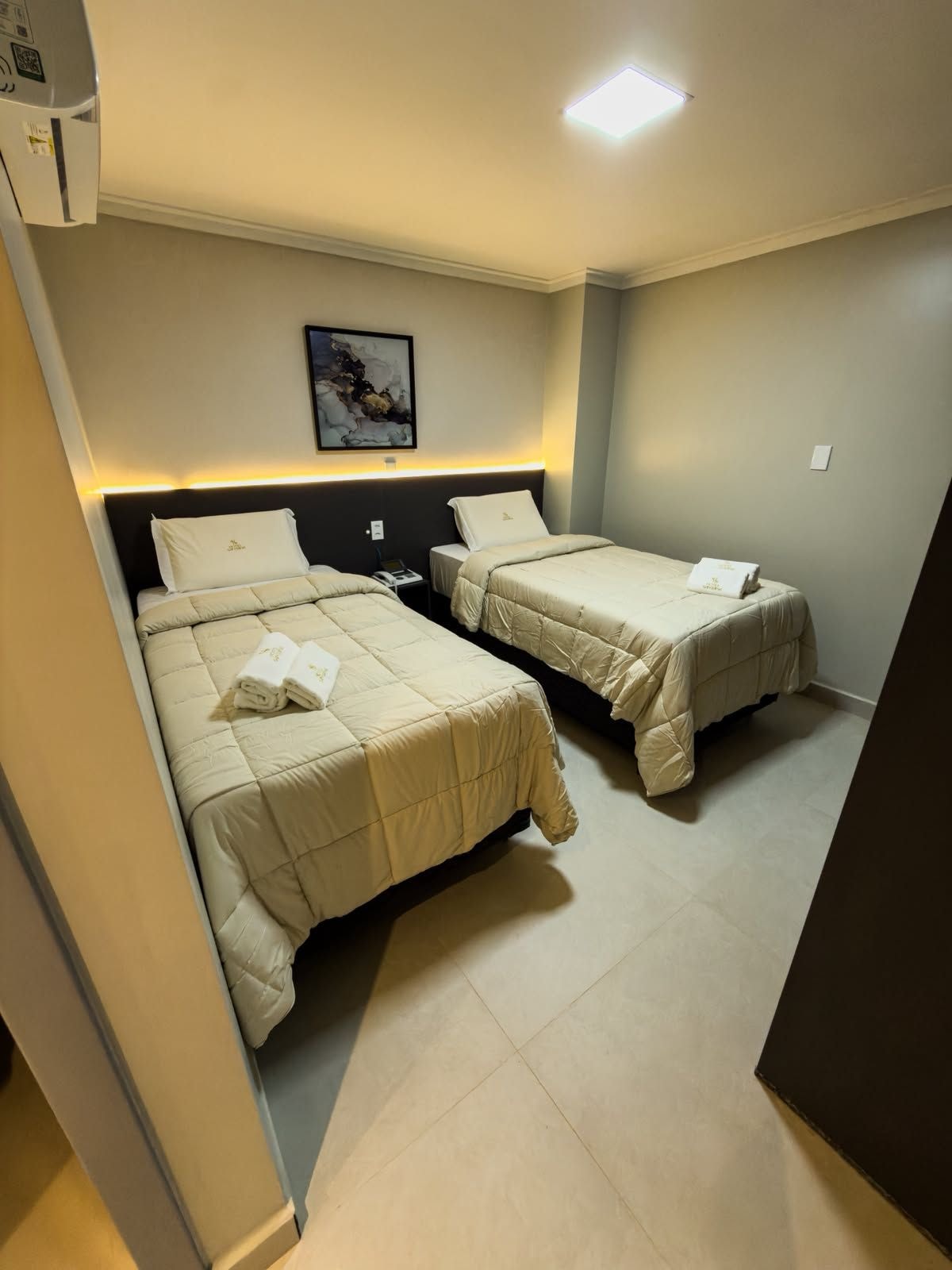 Habitación de hotel con dos camas, una mesita de noche, una obra de arte en la pared y una lámpara en el techo.