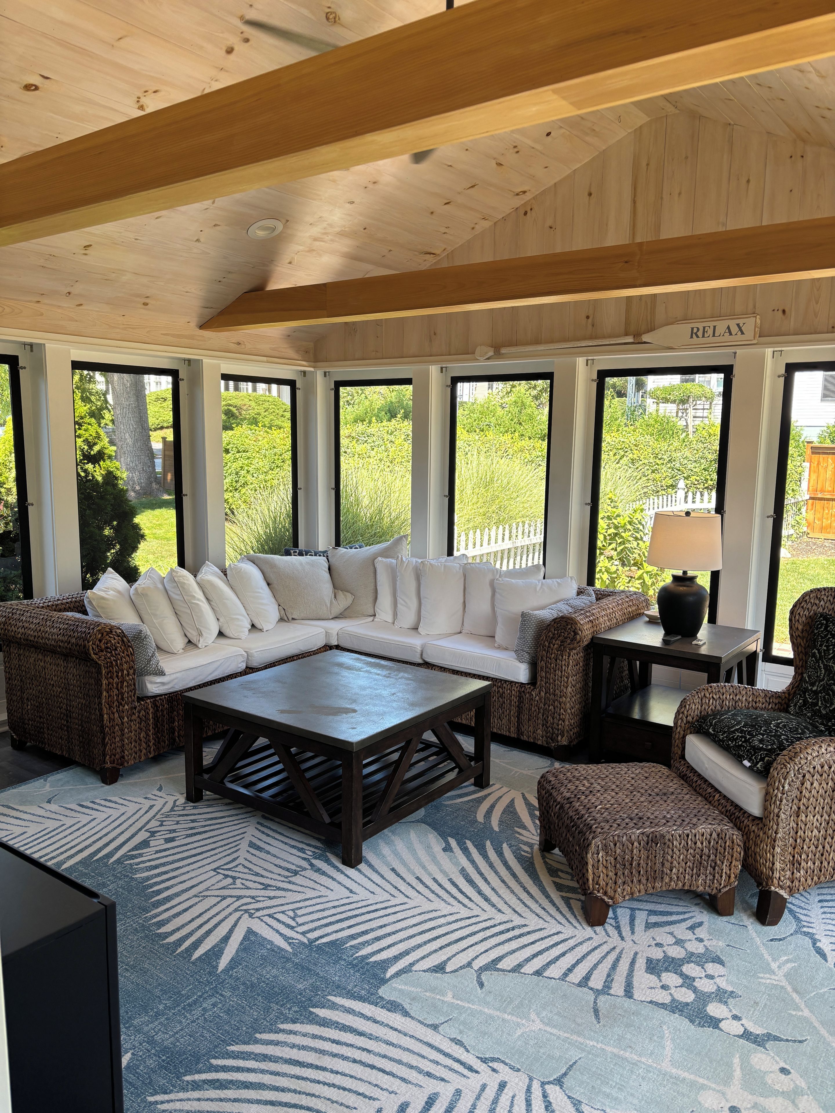 A covered outdoor seating area with a sectional sofa, wicker chairs, a coffee table, and a lamp.
