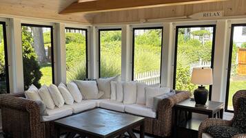 A covered outdoor seating area with a sectional sofa, wicker chairs, a coffee table, and a lamp.