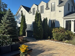 A residential house with a paved driveway, a front porch, and a variety of trees and shrubs. - Historic Carriage House in Downtown Mystic, CT (Mystic)
