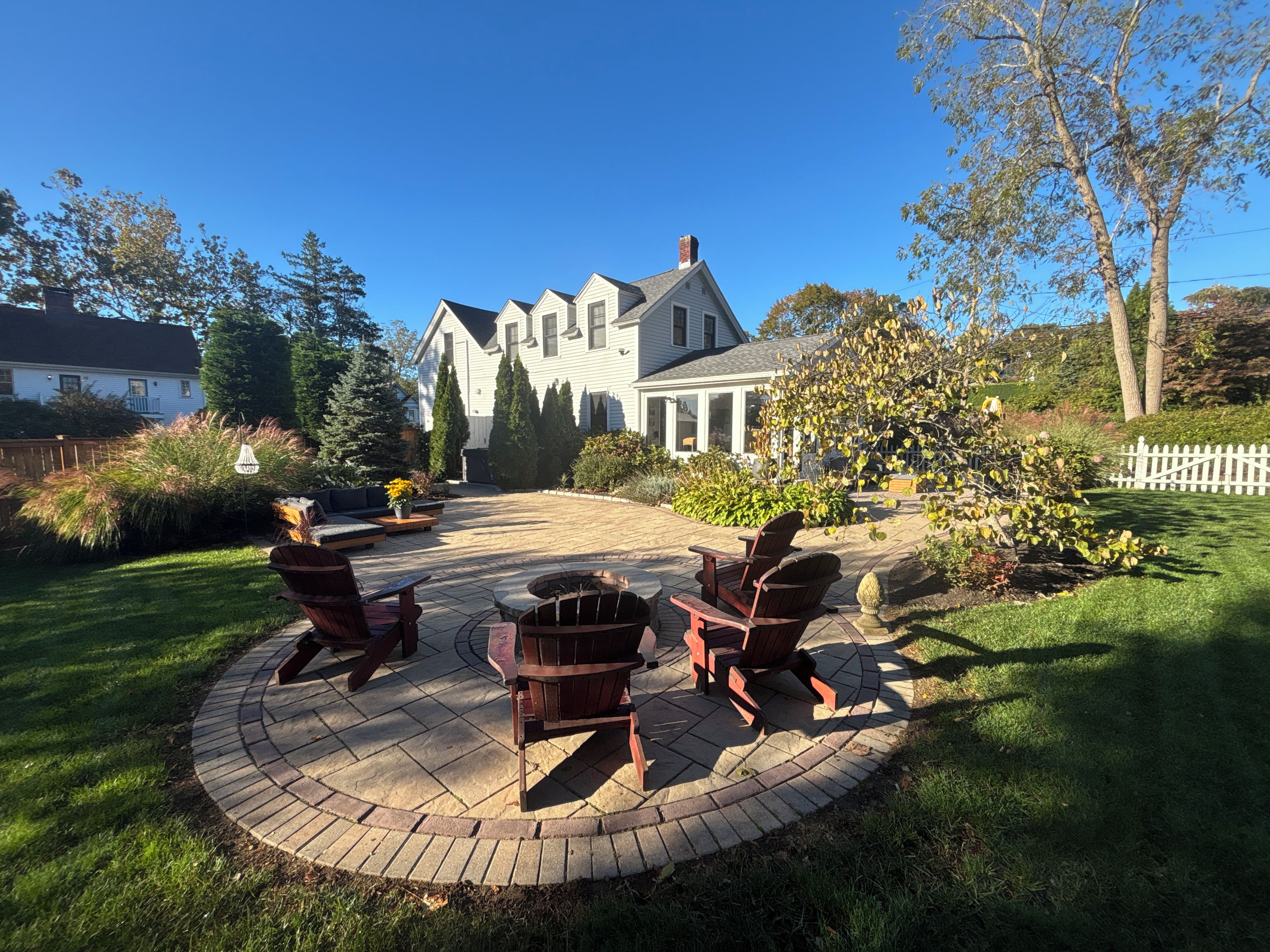 A patio with outdoor seating and a fire pit, surrounded by a well-maintained lawn and trees.