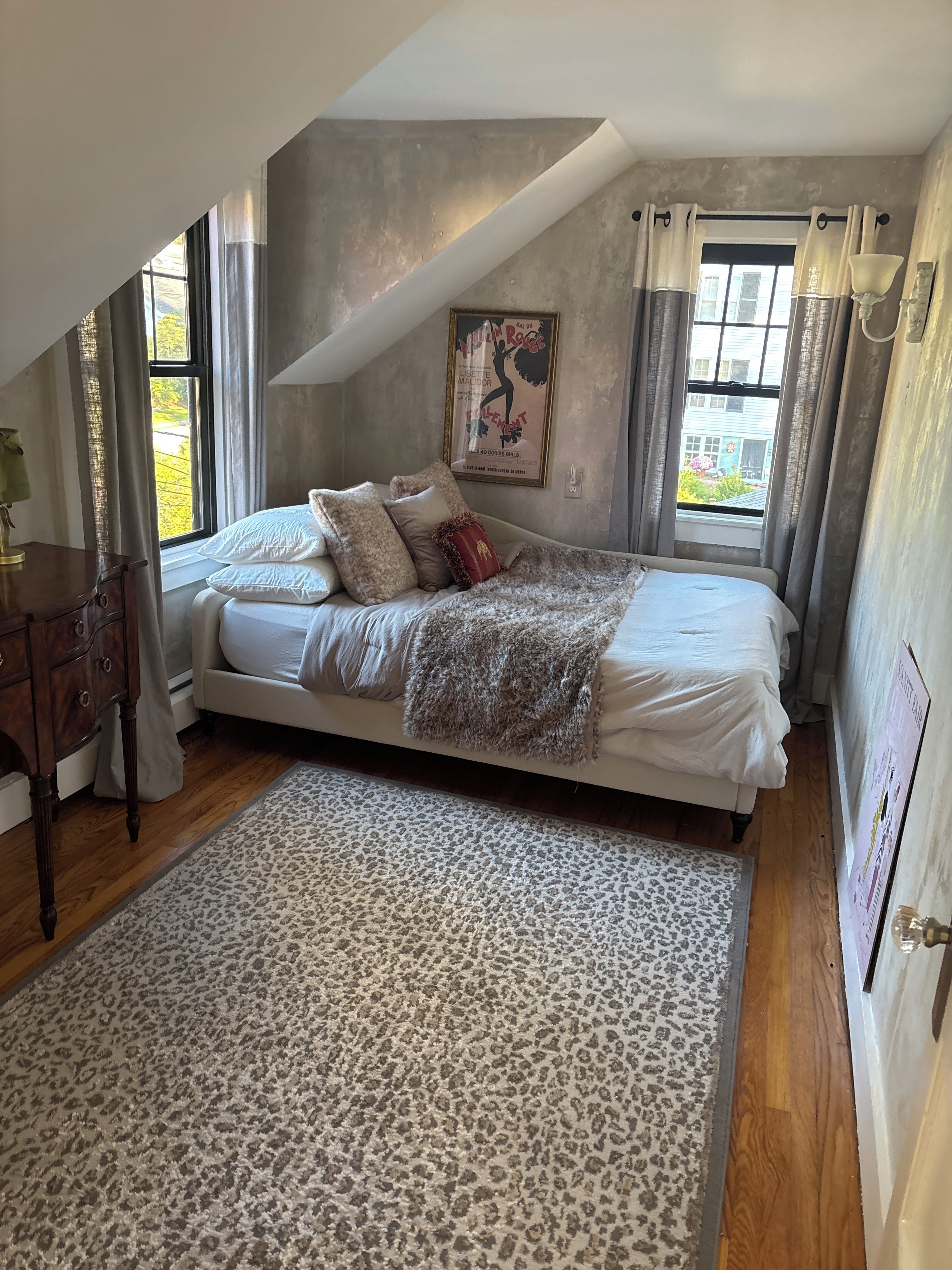 A bedroom with a bed, a dresser, a rug, and a poster on the wall.