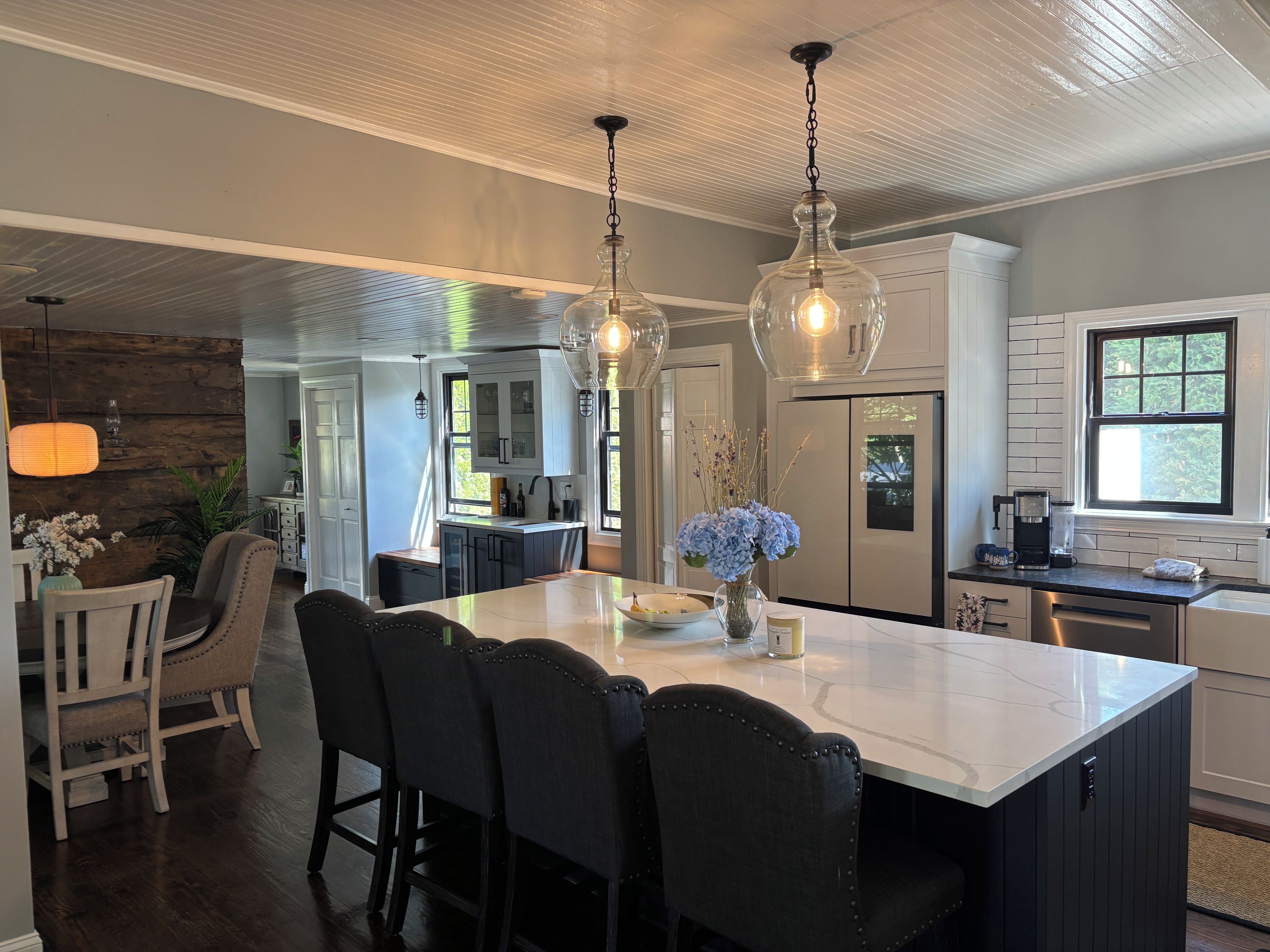 A modern kitchen with a large island, pendant lighting, and a refrigerator.