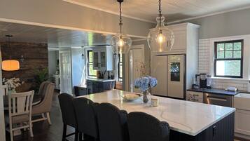 A modern kitchen with a large island, pendant lighting, and a refrigerator.