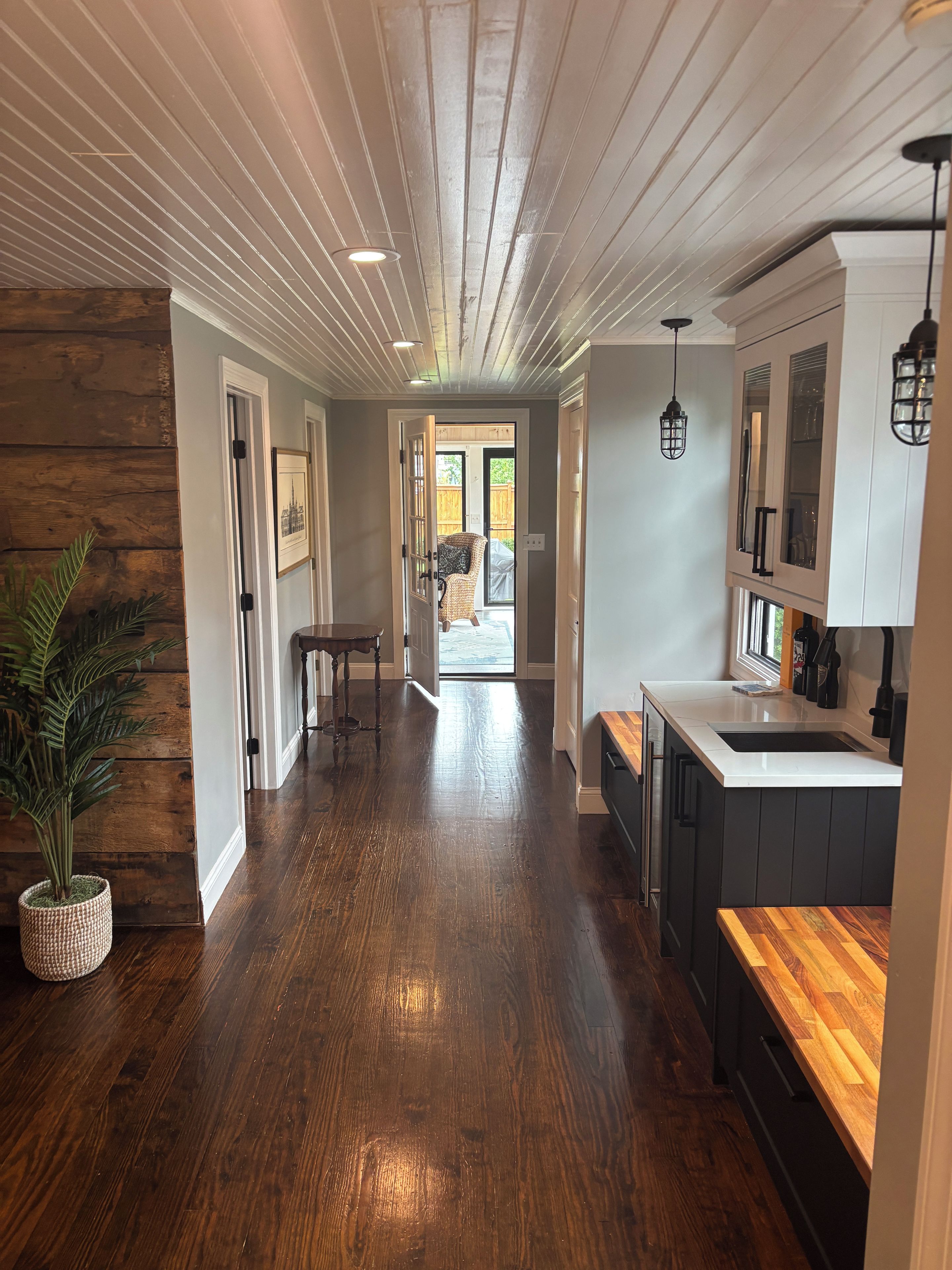 A hallway with wooden flooring leading to a kitchen area with a sink and cabinets.