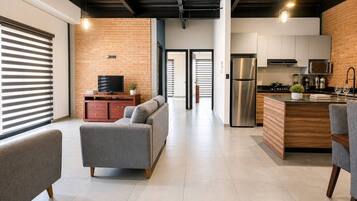 A modern kitchen with stainless steel appliances, a grey sofa, and a wooden dining table.