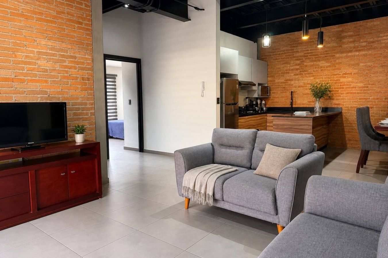 A modern living room with a grey sofa, a flat-screen TV, and a wooden entertainment unit.