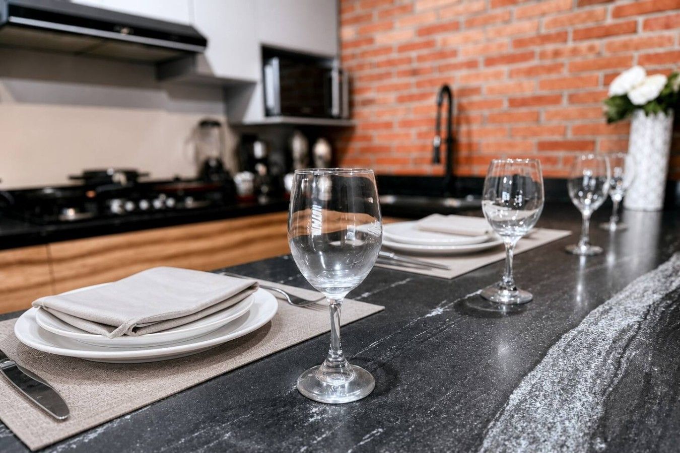 A kitchen counter with wine glasses, plates, and cutlery.