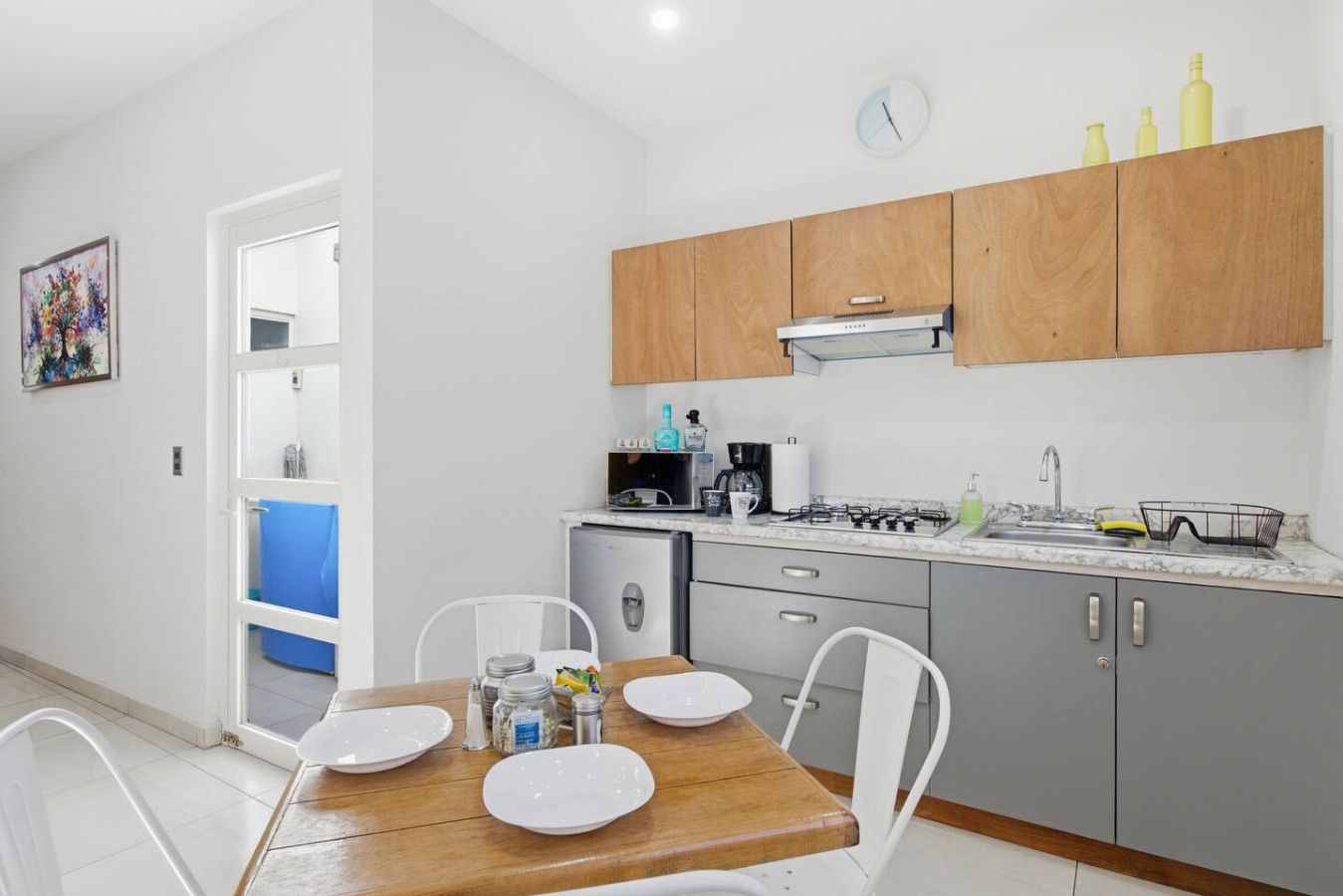 A compact kitchen with wooden cabinets, a gas stove, a microwave, and a sink. There is a dining table with chairs and a blue towel hanging on the door.