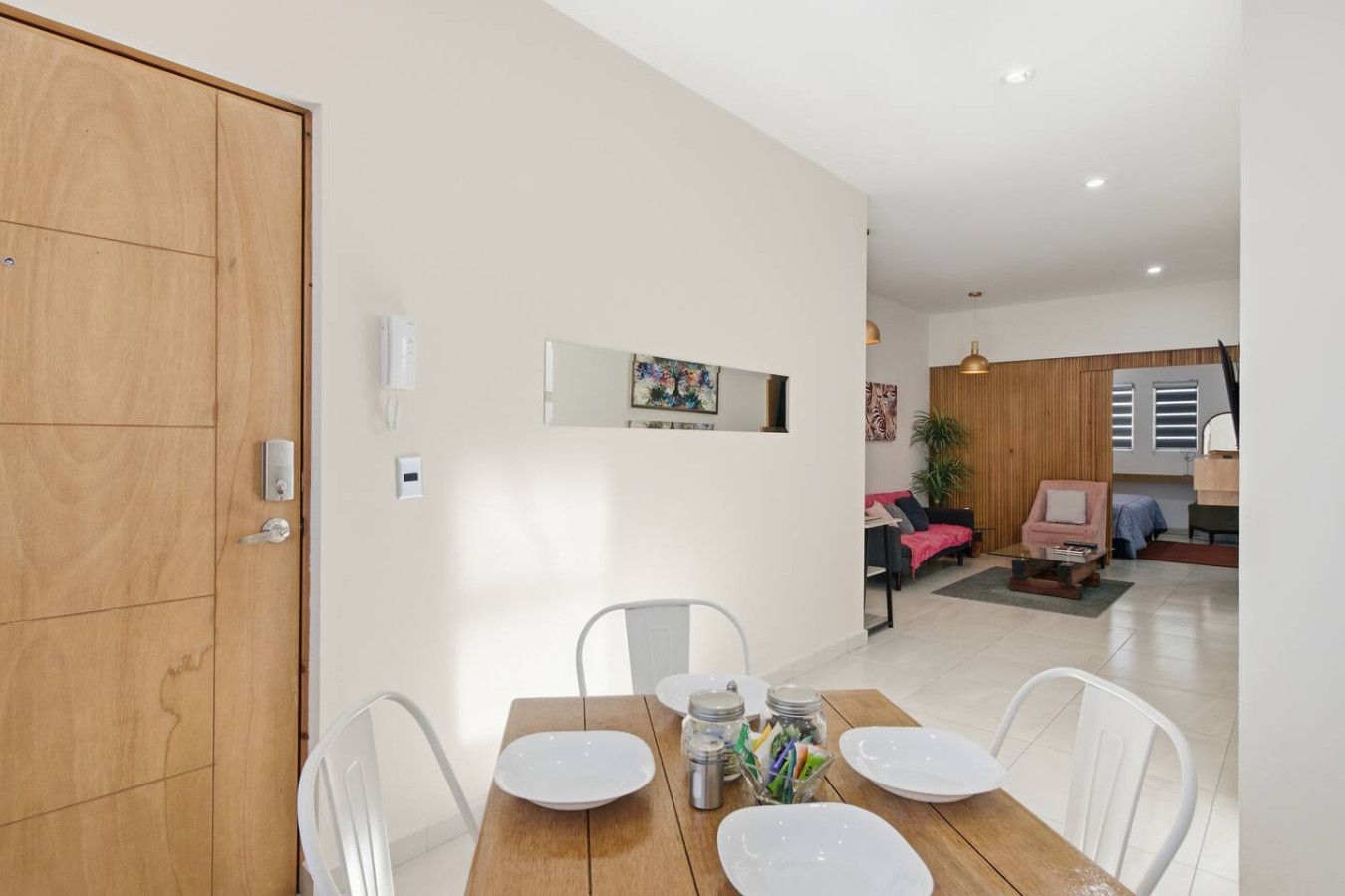 Un coin repas avec une table en bois, des chaises blanches et une petite table d’appoint sur laquelle sont disposés des condiments.