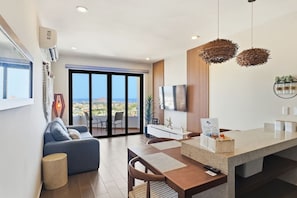 A modern living room with a sofa, a dining area with a table, and a large sliding glass door leading to a balcony with a city view. - Ocean & Old Town views | Rooftop pool (Mazatlán)