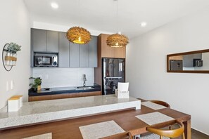 Een moderne keuken met een centraal eiland, roestvrijstalen apparatuur en twee hangende lampen.