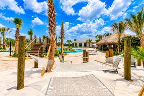 A resort pool area with a thatched-roof structure, palm trees, and a hammock. - 4BR Near Disney, Private Heated Pool, Storey Lake Resort, Sleeps 12 (Kissimmee)