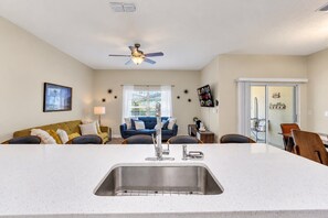 A modern kitchen with a central island, a dining area with chairs, a sofa, and a ceiling fan. - 4BR Near Disney, Private Heated Pool, Storey Lake Resort, Sleeps 12 (Kissimmee)
