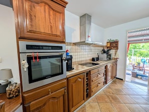 Eine Küche mit Holzausstattung, einem Einbauofen, einer Kaffeemaschine und einer gefliesten Spritzschutzwand.