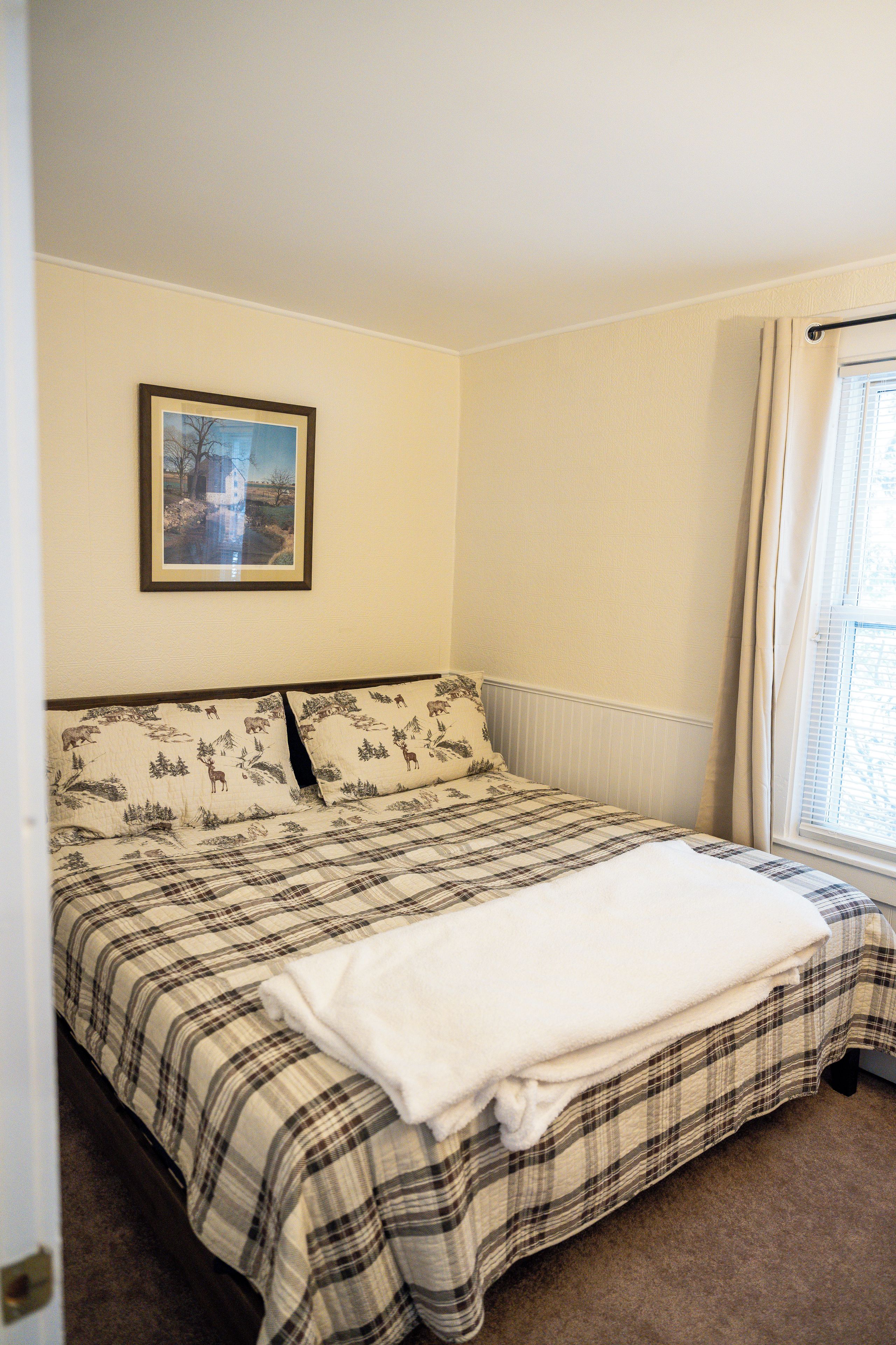 Una camera da letto con un letto, una finestra con tende, un termosifone e un quadro appeso al muro.