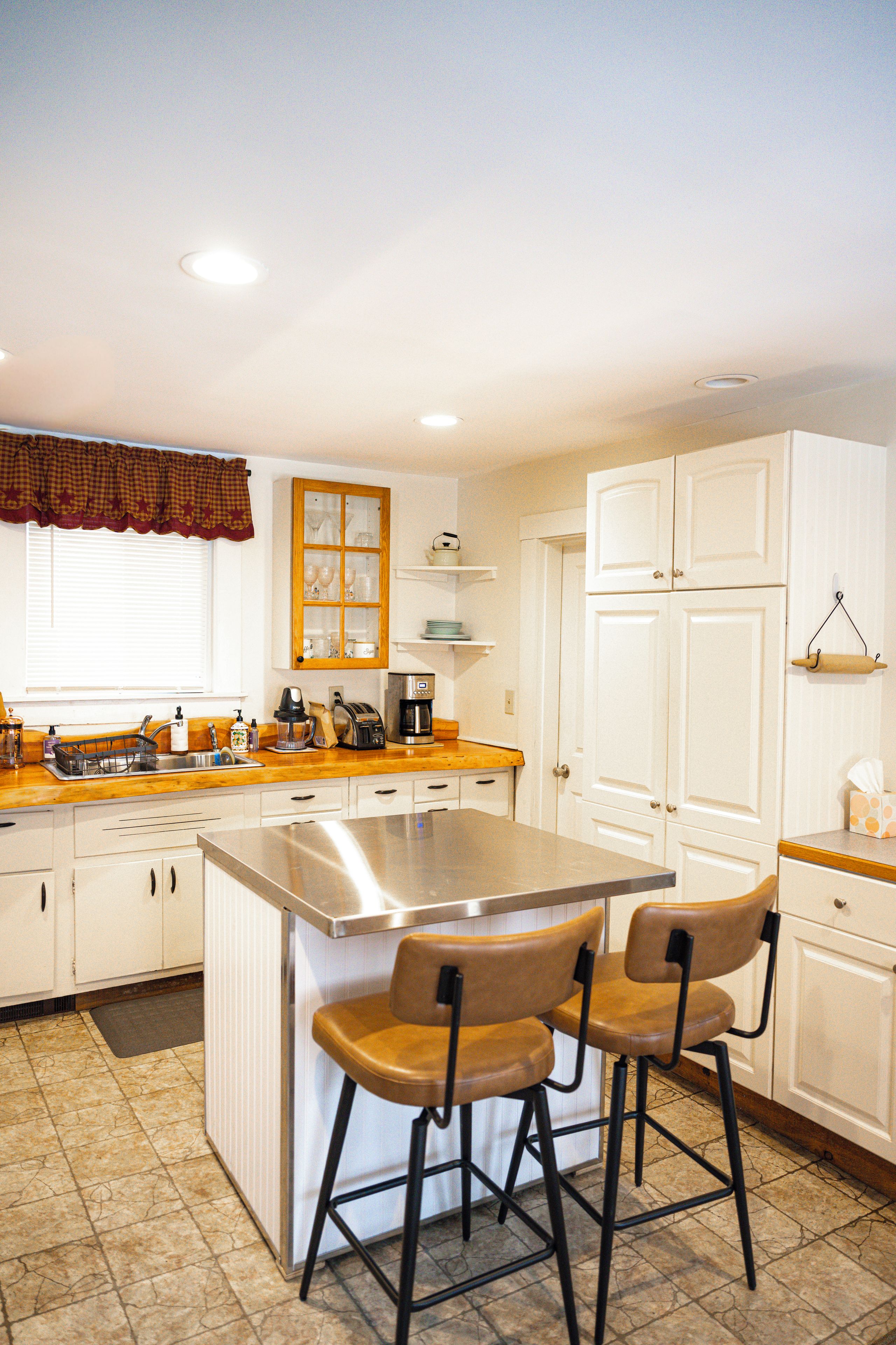 A kitchen with white cabinets, a stainless steel island, and two bar stools.