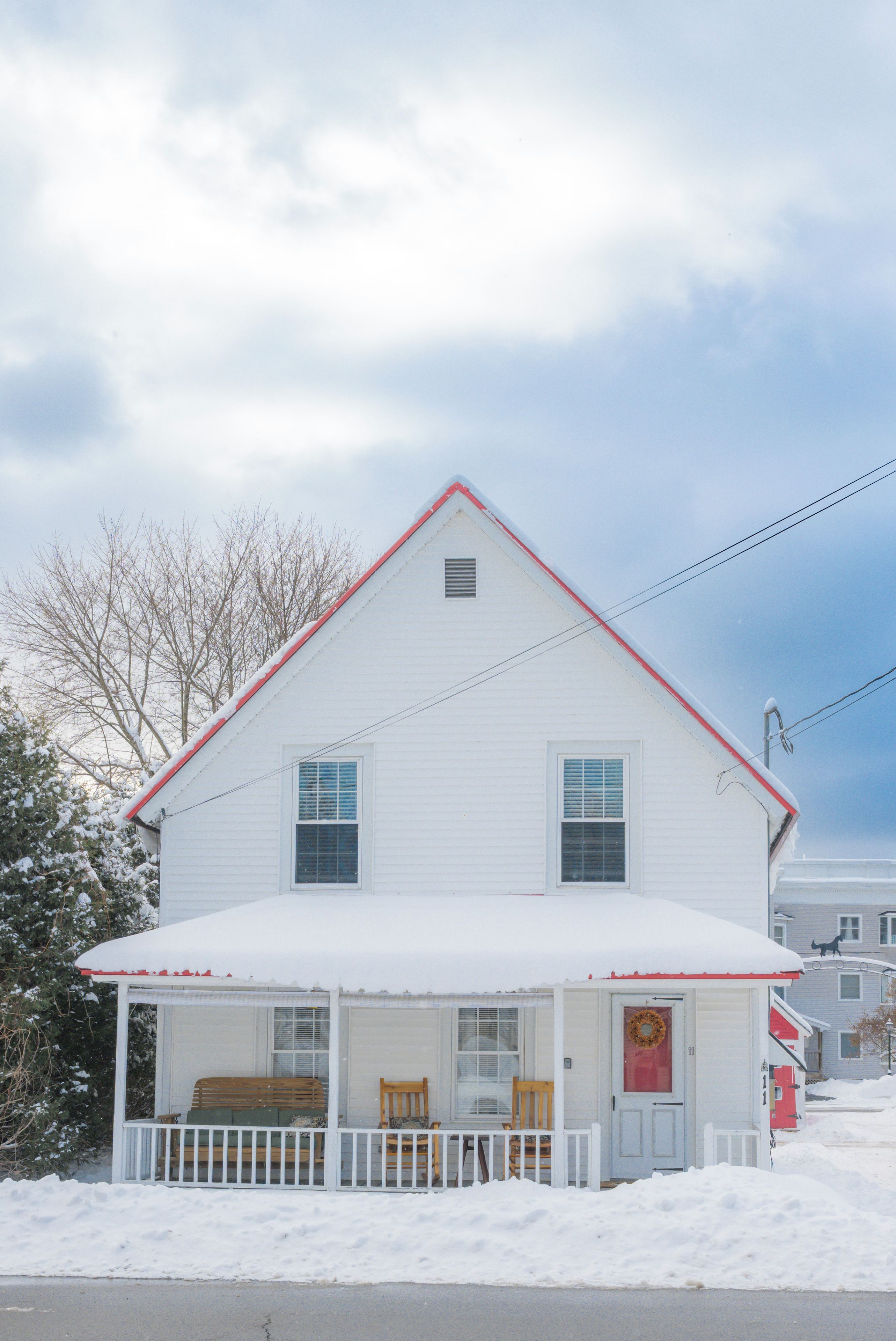 A white house with a red roof, a porch with a bench, and a door with a wreath.