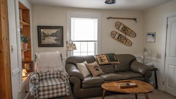 A living room with a brown leather sofa, a plaid armchair, a wooden coffee table, and a window with blinds.