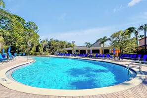 Una piscina circolare con acqua azzurra, circondata da poltrone da relax blu e un percorso pedonale in mattoni.