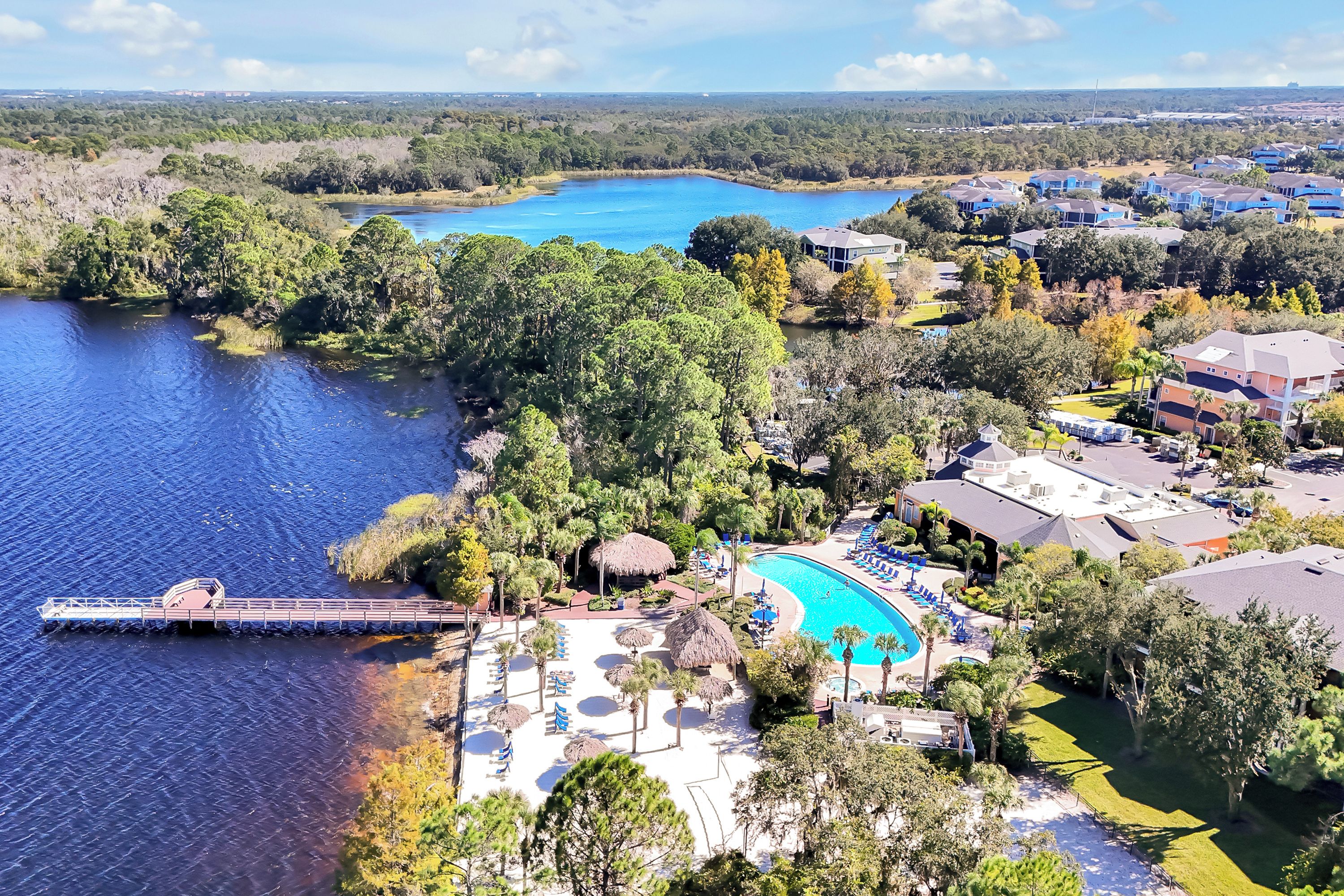 An aerial view of a resort with a swimming pool, a dock, and a lake.