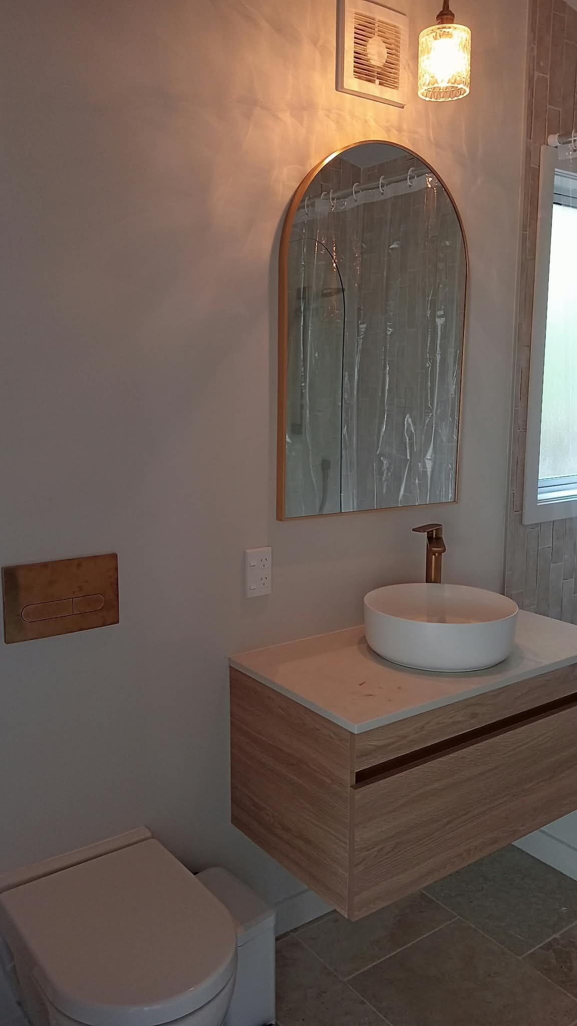 Ein Badezimmer mit einer weißen Toilette, einem runden Waschbecken mit einem hölzernen Waschtisch und einem großen Spiegel über dem Waschbecken.